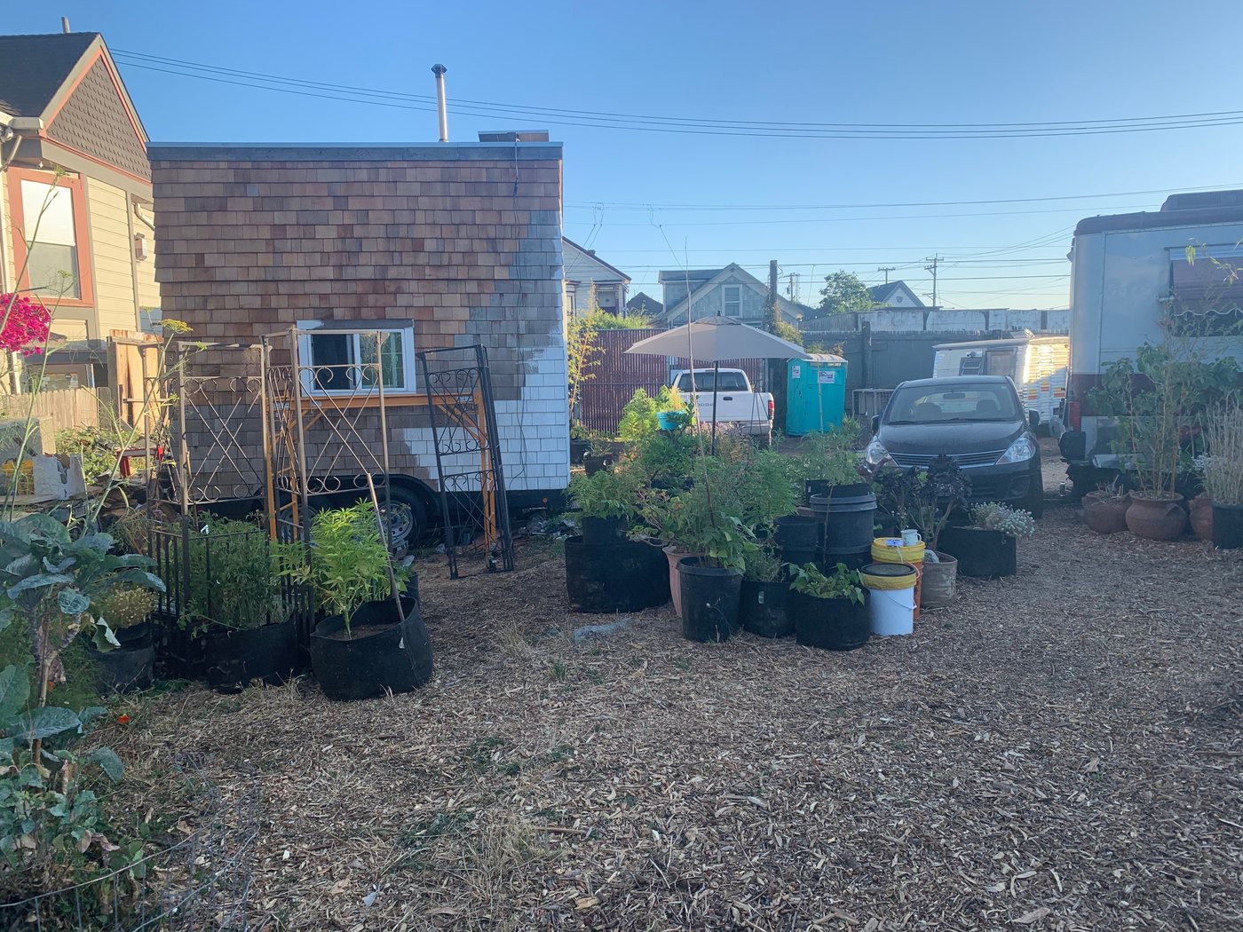 A shingled tiny home on wheels among the garden beds